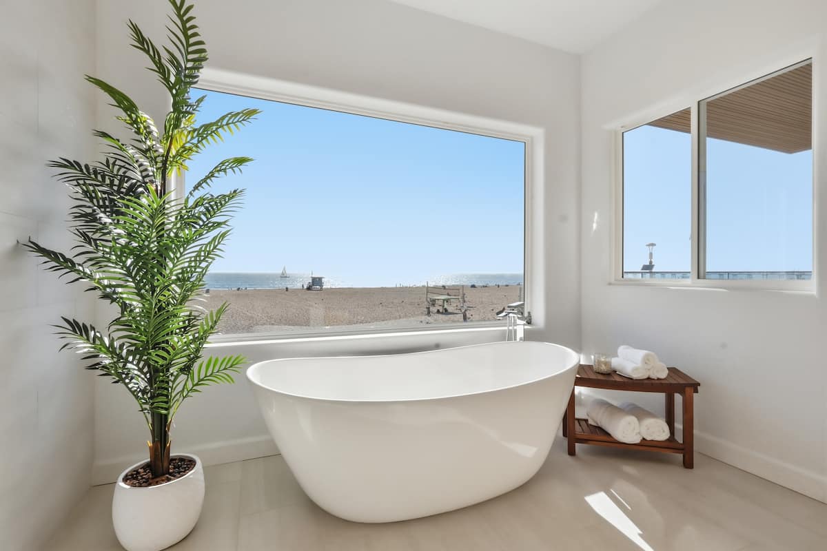 Freestanding soaking tub beneath a wide window over the beach